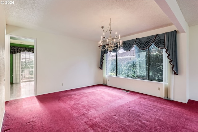 carpeted empty room with a chandelier, a healthy amount of sunlight, and a textured ceiling