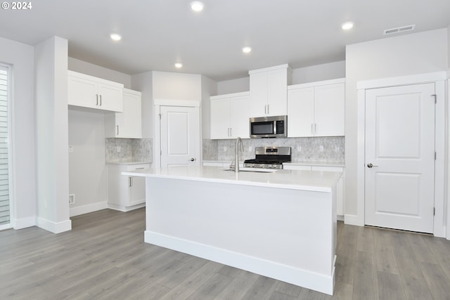 kitchen with appliances with stainless steel finishes, white cabinets, a kitchen island with sink, and light hardwood / wood-style floors