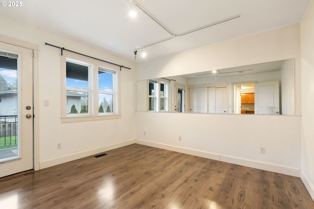 empty room with hardwood / wood-style flooring, rail lighting, and a wealth of natural light