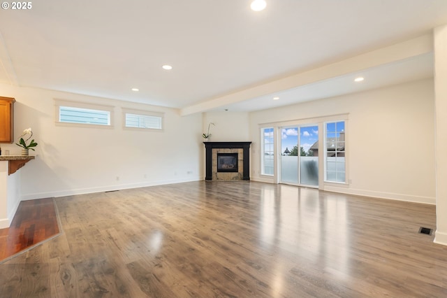 unfurnished living room featuring light wood-type flooring, a tiled fireplace, and beamed ceiling