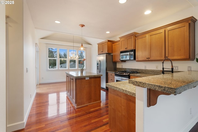 kitchen with appliances with stainless steel finishes, a kitchen bar, sink, hanging light fixtures, and dark hardwood / wood-style floors