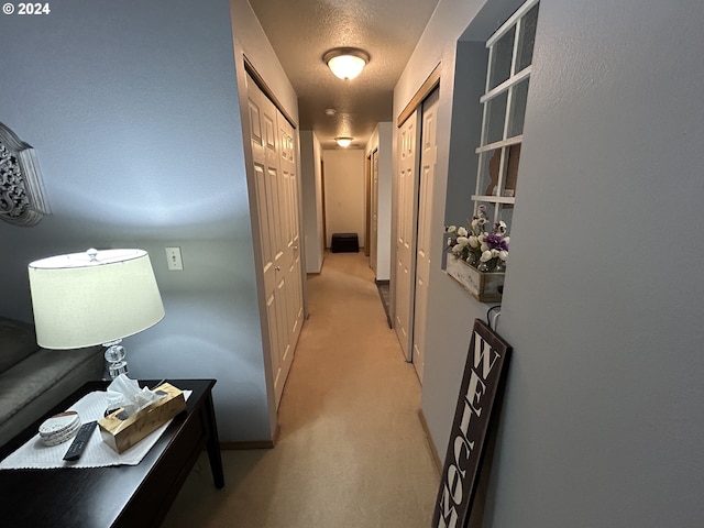 hallway featuring light carpet and a textured ceiling