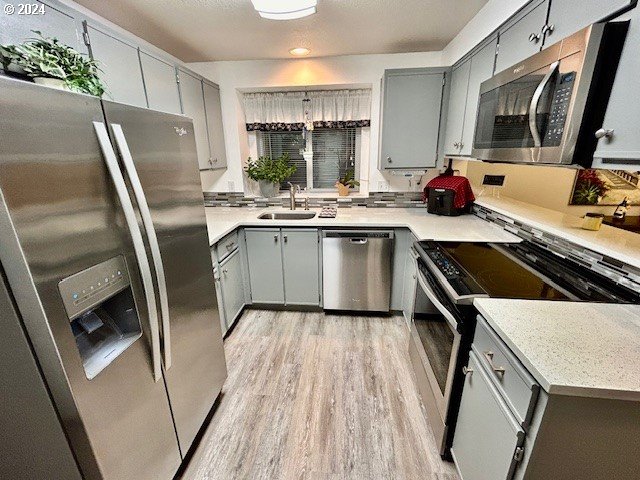 kitchen featuring appliances with stainless steel finishes, light wood-type flooring, gray cabinetry, and sink