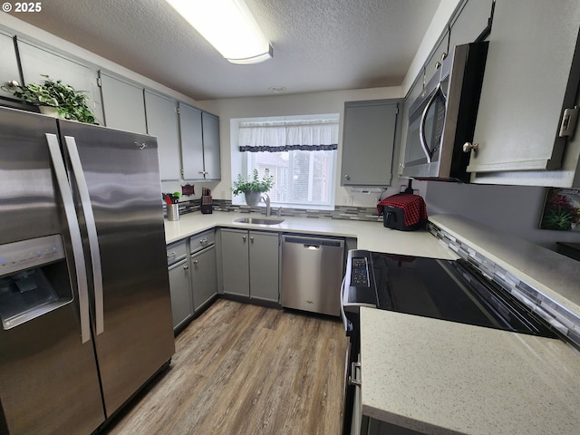 kitchen with appliances with stainless steel finishes, light wood-type flooring, a textured ceiling, gray cabinets, and sink