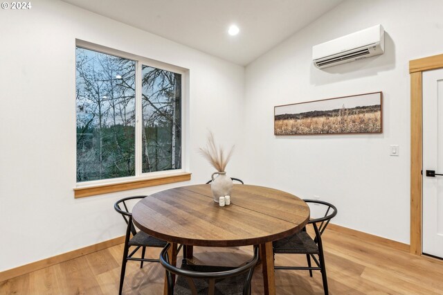 dining room with an AC wall unit, light hardwood / wood-style floors, and vaulted ceiling