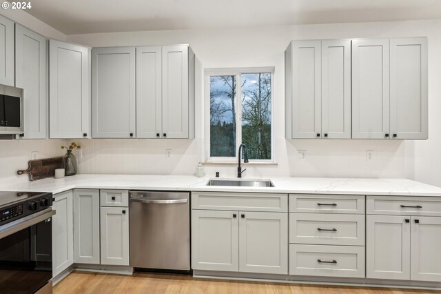 kitchen with light hardwood / wood-style floors, light stone counters, sink, and appliances with stainless steel finishes