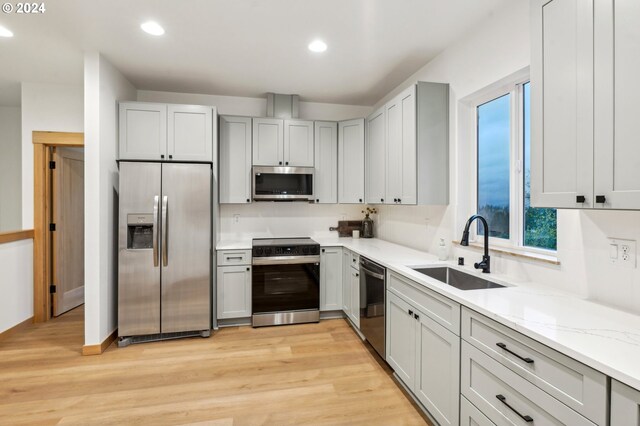 kitchen with light stone counters, sink, stainless steel appliances, and light hardwood / wood-style flooring