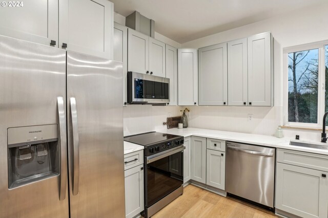 kitchen with light stone countertops, appliances with stainless steel finishes, gray cabinetry, sink, and light hardwood / wood-style floors