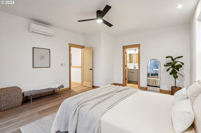 bedroom featuring a wall mounted air conditioner, ensuite bathroom, ceiling fan, sink, and light hardwood / wood-style flooring