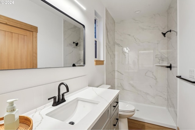 bathroom with hardwood / wood-style floors, vanity, toilet, and tiled shower