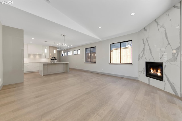 unfurnished living room with a high end fireplace, a healthy amount of sunlight, lofted ceiling, and light wood-type flooring