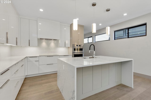 kitchen with stainless steel double oven, white cabinetry, a kitchen island with sink, and sink