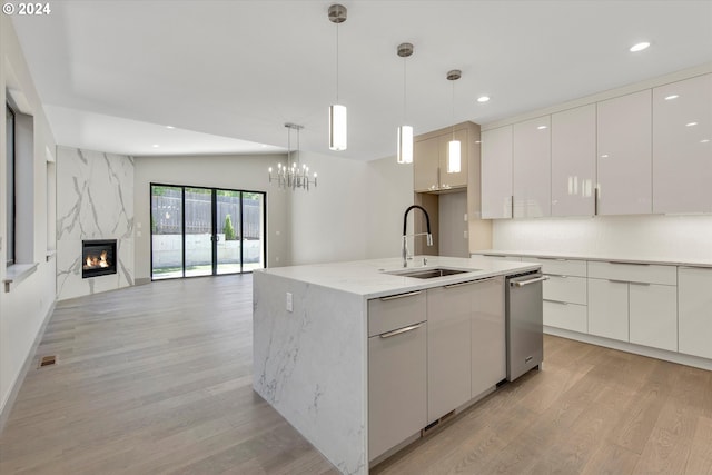 kitchen featuring a high end fireplace, sink, decorative light fixtures, white cabinets, and an island with sink