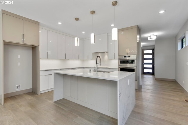 kitchen with a kitchen island with sink, sink, decorative light fixtures, light hardwood / wood-style flooring, and white cabinets