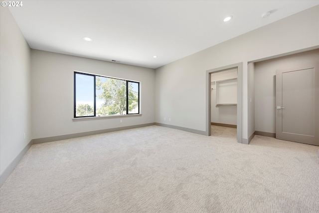 unfurnished bedroom featuring a walk in closet, light colored carpet, and a closet