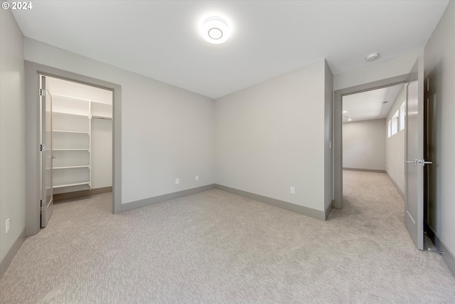 unfurnished bedroom with a spacious closet, a closet, and light colored carpet