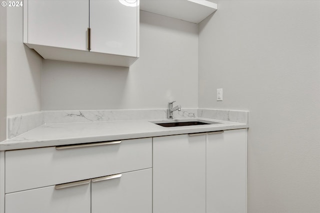 kitchen with light stone countertops, white cabinetry, and sink