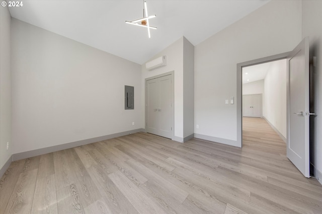 unfurnished bedroom featuring electric panel, light hardwood / wood-style flooring, a wall mounted AC, and vaulted ceiling