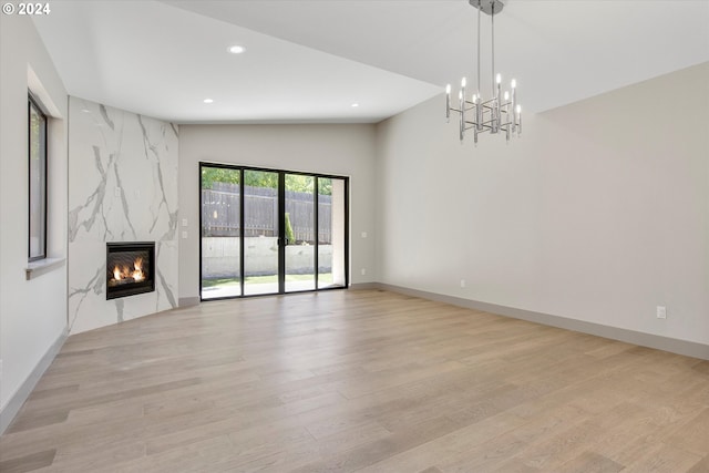 unfurnished living room featuring a chandelier, light hardwood / wood-style flooring, lofted ceiling, and a premium fireplace