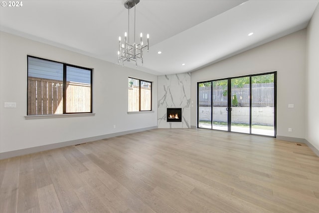 unfurnished living room with light wood-type flooring, an inviting chandelier, vaulted ceiling, and a premium fireplace