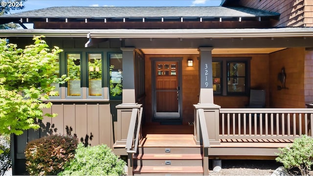 entrance to property with board and batten siding, covered porch, and roof with shingles