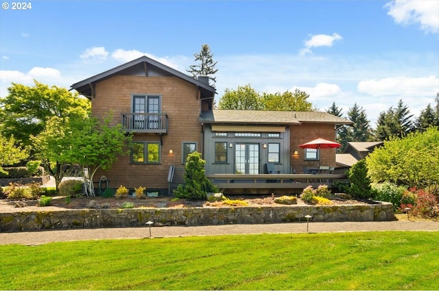 rear view of property with a balcony, a lawn, and french doors