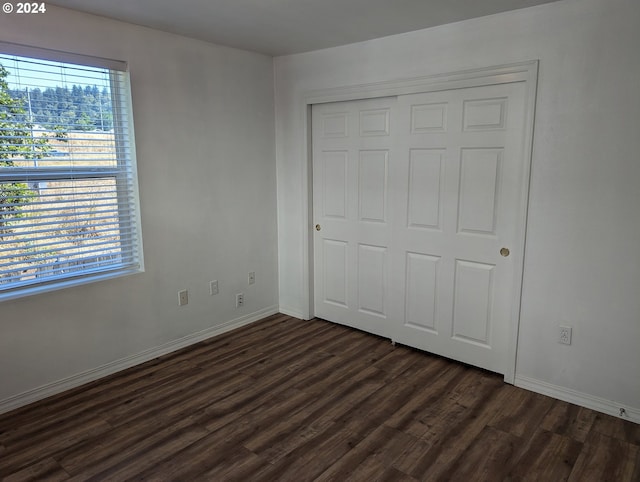 unfurnished bedroom with dark wood-style flooring, a closet, and baseboards