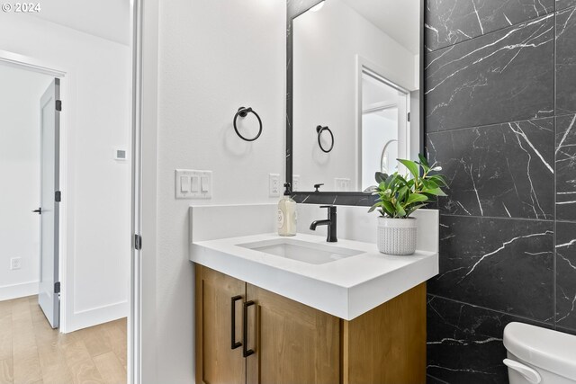 bathroom with hardwood / wood-style floors, vanity, toilet, and tile walls