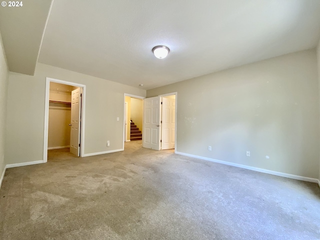 unfurnished bedroom featuring a spacious closet, light colored carpet, and a closet