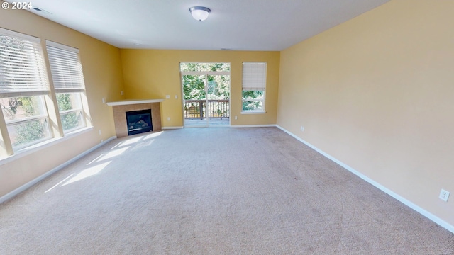 unfurnished living room with a tile fireplace, a healthy amount of sunlight, and light carpet