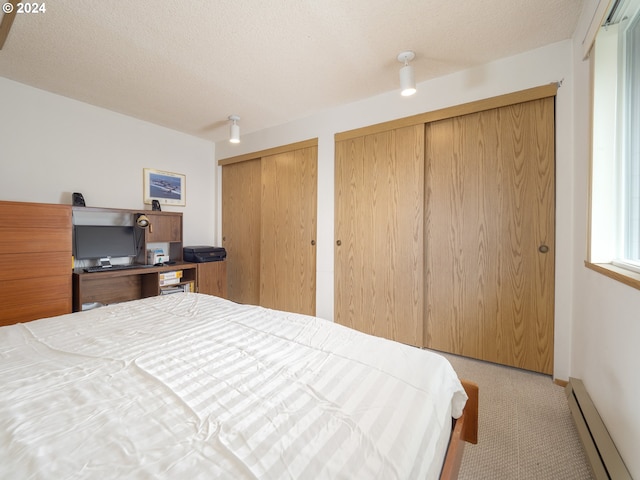 carpeted bedroom with a textured ceiling, multiple closets, and a baseboard heating unit