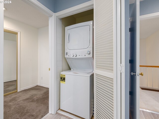 clothes washing area with stacked washer / drying machine and light colored carpet