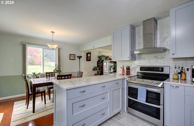 kitchen featuring a peninsula, double oven range, wall chimney exhaust hood, light wood finished floors, and tasteful backsplash