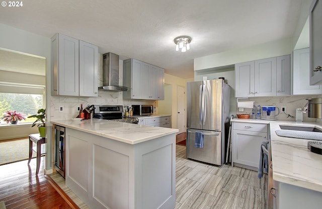 kitchen featuring stainless steel appliances, light stone counters, wall chimney exhaust hood, and tasteful backsplash