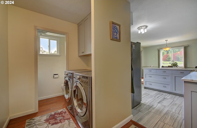 clothes washing area featuring light wood-type flooring, cabinet space, baseboards, and washer and dryer