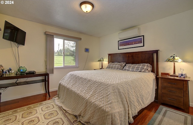 bedroom featuring a textured ceiling, baseboards, dark wood-type flooring, and a wall mounted AC