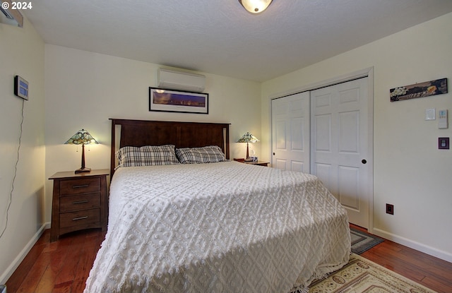 bedroom with a closet, a wall mounted air conditioner, wood-type flooring, and baseboards