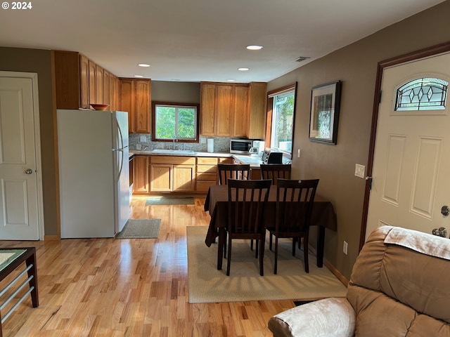 kitchen with light wood-type flooring, kitchen peninsula, white refrigerator, sink, and backsplash