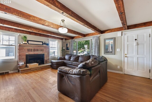 living room featuring wood-type flooring, beamed ceiling, and a brick fireplace