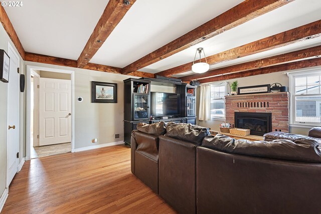 living room featuring beam ceiling, a brick fireplace, and light hardwood / wood-style flooring