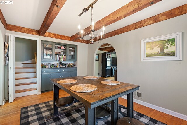 dining space with beam ceiling, a notable chandelier, and light hardwood / wood-style flooring