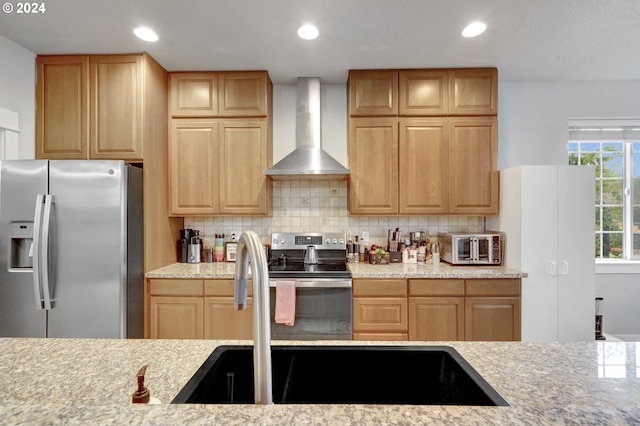 kitchen featuring wall chimney range hood, decorative backsplash, appliances with stainless steel finishes, light stone countertops, and sink