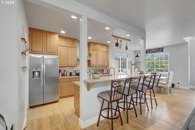 kitchen featuring a breakfast bar area, stainless steel fridge, light stone counters, light hardwood / wood-style floors, and tasteful backsplash