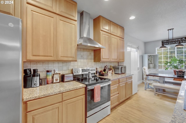 kitchen featuring light brown cabinetry, light hardwood / wood-style floors, stainless steel appliances, wall chimney exhaust hood, and pendant lighting