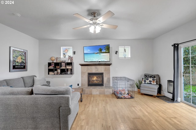 living room featuring a tiled fireplace, light wood-type flooring, and ceiling fan