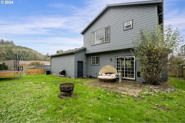 rear view of house featuring a mountain view, an outdoor fire pit, a lawn, and a trampoline