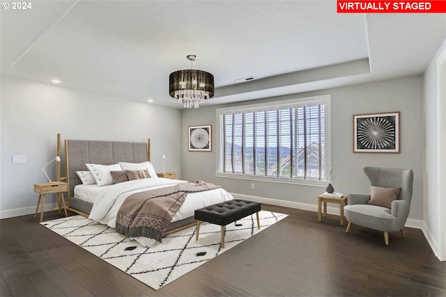 bedroom featuring dark hardwood / wood-style floors, a raised ceiling, and a notable chandelier