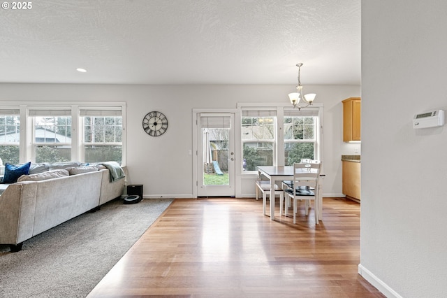 living room with a chandelier, light wood-type flooring, a textured ceiling, and baseboards