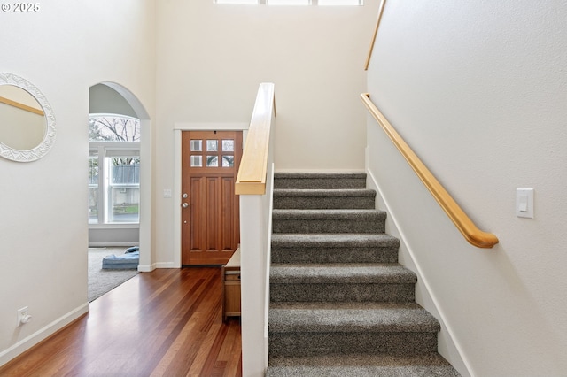 staircase featuring arched walkways, a towering ceiling, baseboards, and wood finished floors