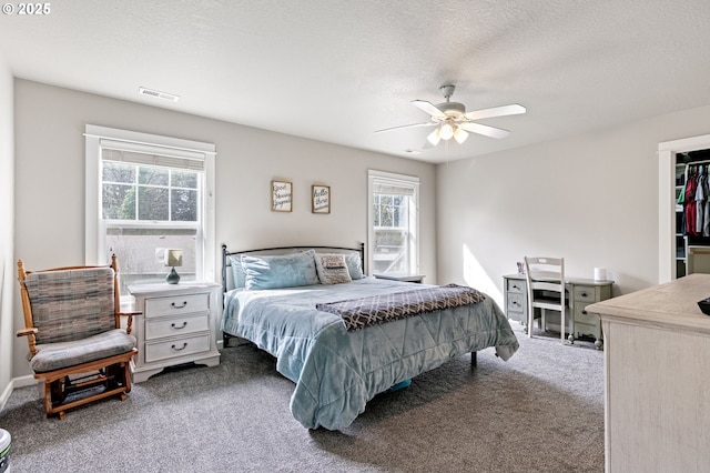 carpeted bedroom with a walk in closet, visible vents, ceiling fan, and a textured ceiling